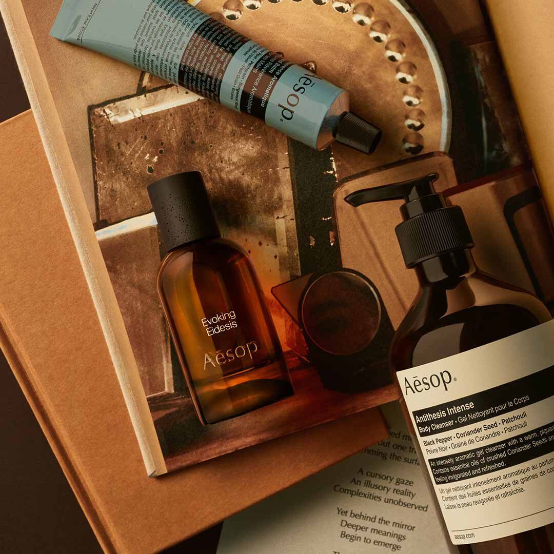 Aesop Evoking Eidesis Flakon mit Pumpspender und blauem Schlauch, arrangiert auf Papieren und Bildern eines Spiegeltabletts.