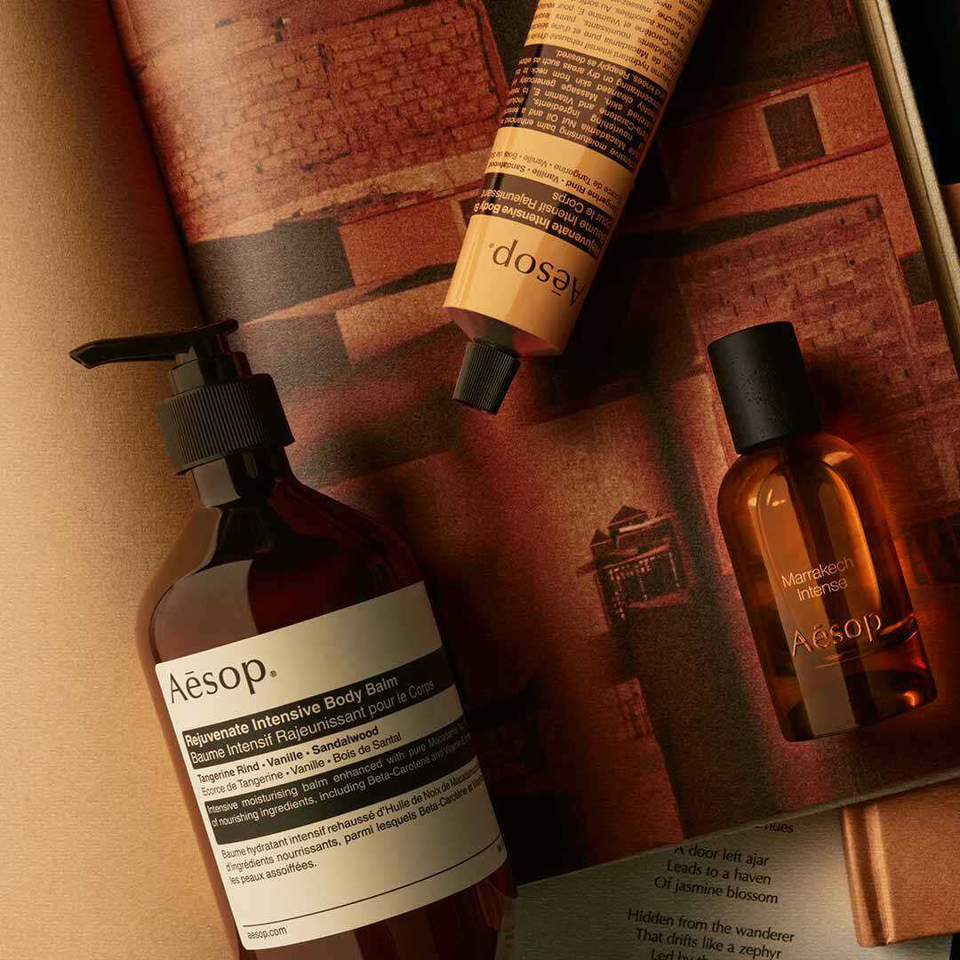 Aesop Marrakech Intense Flakon mit Pumpspender und gelbem Schlauch, arrangiert auf Papieren in warmen Farbtonen.