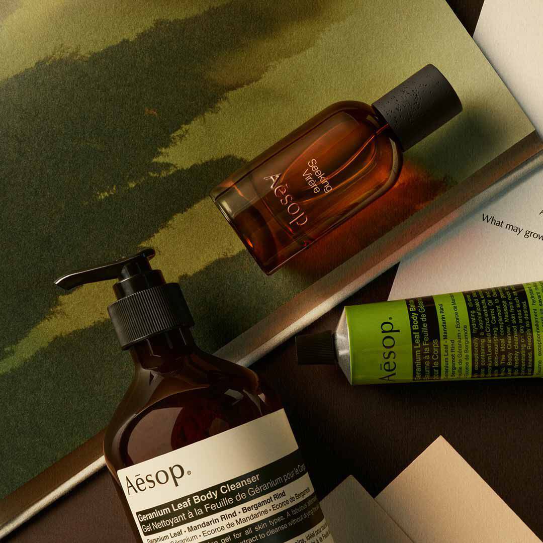 Aesop Seeking Virere Flakon mit Pumpspender und grunem Schlauch, arrangiert auf Papieren mit gemalten Motiven in Gruntonen.