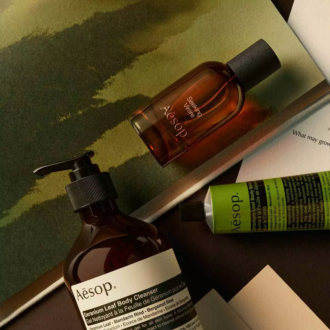 Aesop Seeking Virere Flakon mit Pumpspender und grunem Schlauch, arrangiert auf Papieren mit gemalten Motiven in Gruntonen.