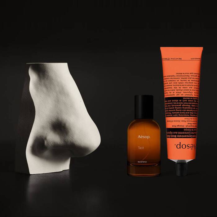 Bernsteinfarbene Parfumflasche und korallenfarbene Handcreme neben einer weißen Skulptur