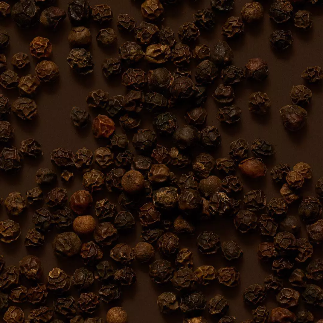 Close-up of peppercorns scattered across a dark brown surface.