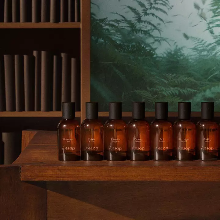 Eine Reihe von Aesop Parfumflaschen aus Bernsteinglas auf einem Holzregal.