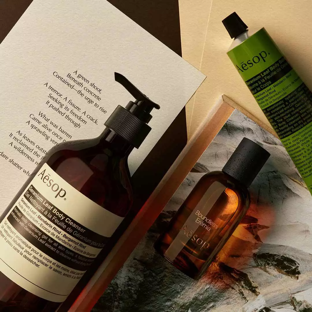 Aesop Boundless Eremia Flakon mit Pumpspender und grunem Schlauch, arrangiert auf Papieren und einem Steinbild.